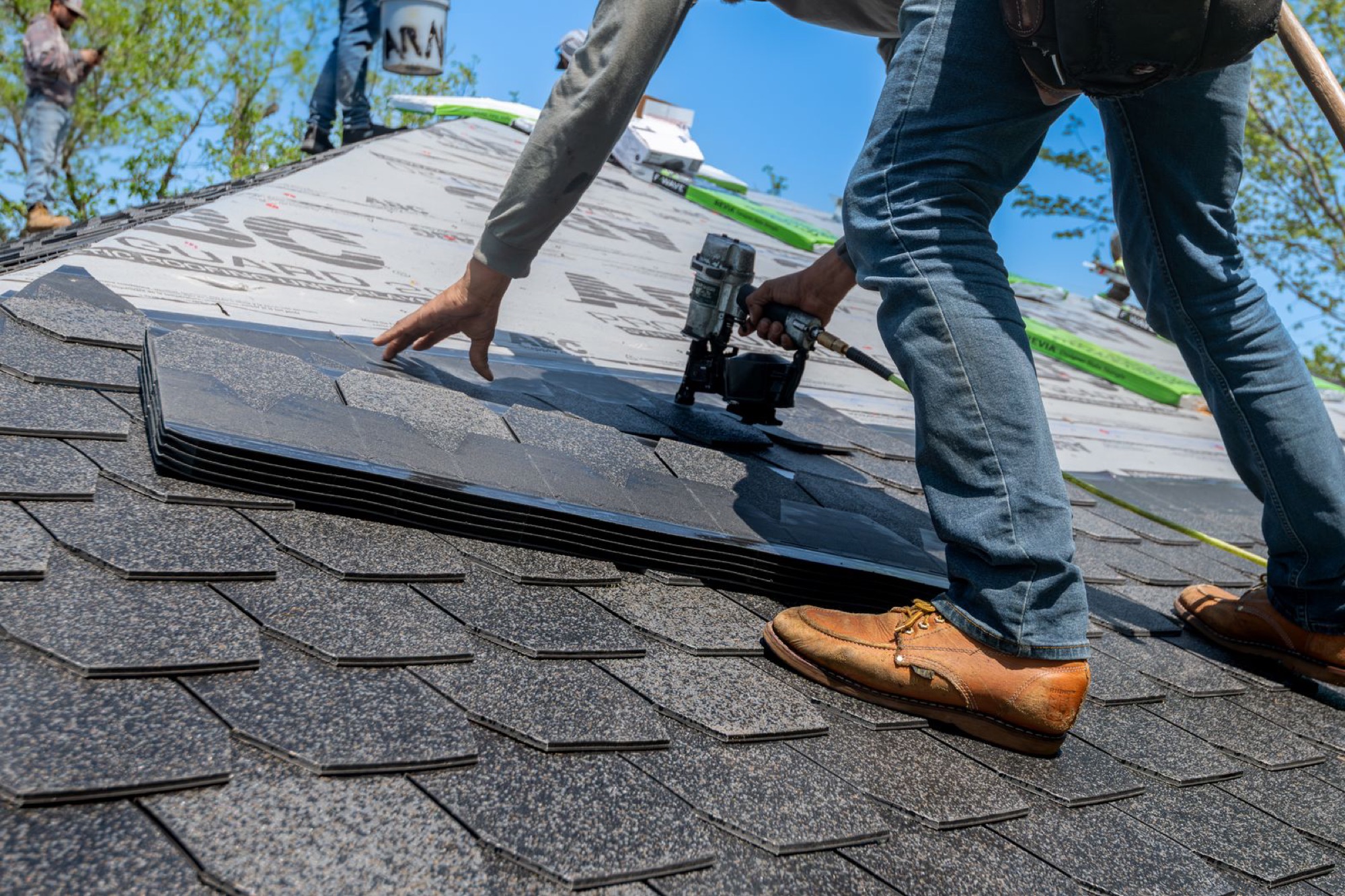 Roofer nailing down new asphalt shingles on a residential roof